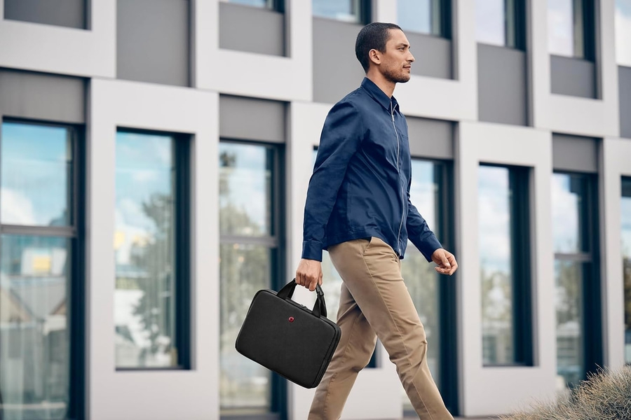 Mann mit schwarzer Tasche geht an einem Gebäude vorbei, blaues Outfit
