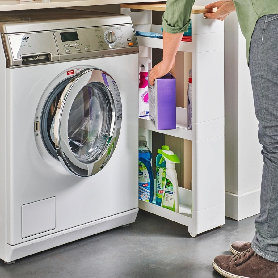 Waschmaschine und Reinigungsmittel. Person greift nach Box. Weißer Schrank mit Rollen.