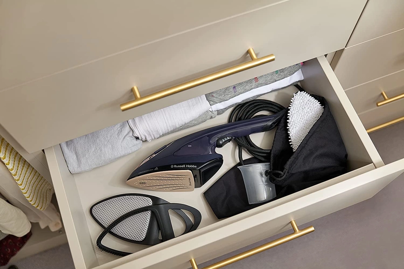 Offene Schublade mit Bügeleisen, Zubehör und Kleidung. Goldene Griffe.