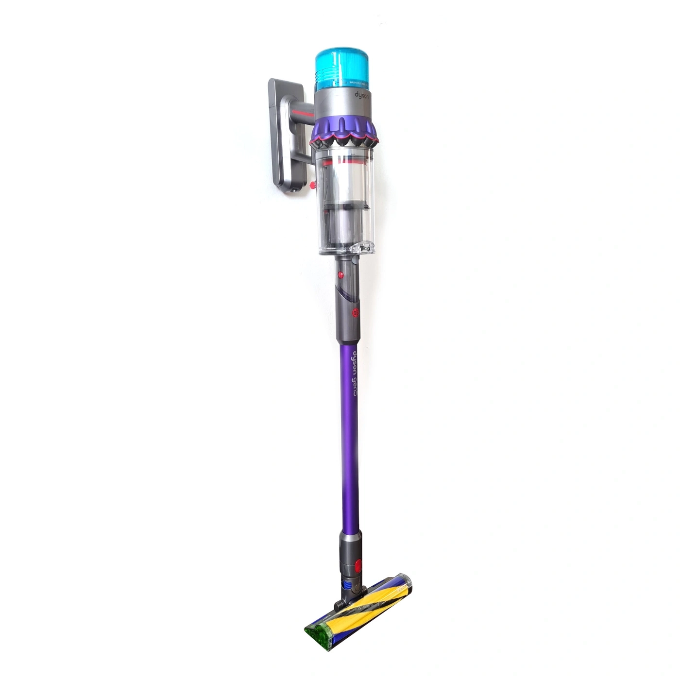 Ein violetter Dyson-Staubsauger mit Wandhalterung und Bürstenkopf steht vor weißem Hintergrund.