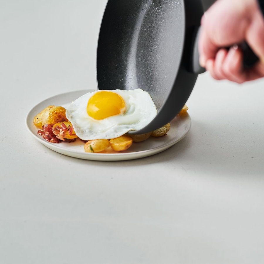 Ein Teller mit Spiegelei, Kartoffeln und Speck, serviert mit einer Pfanne.