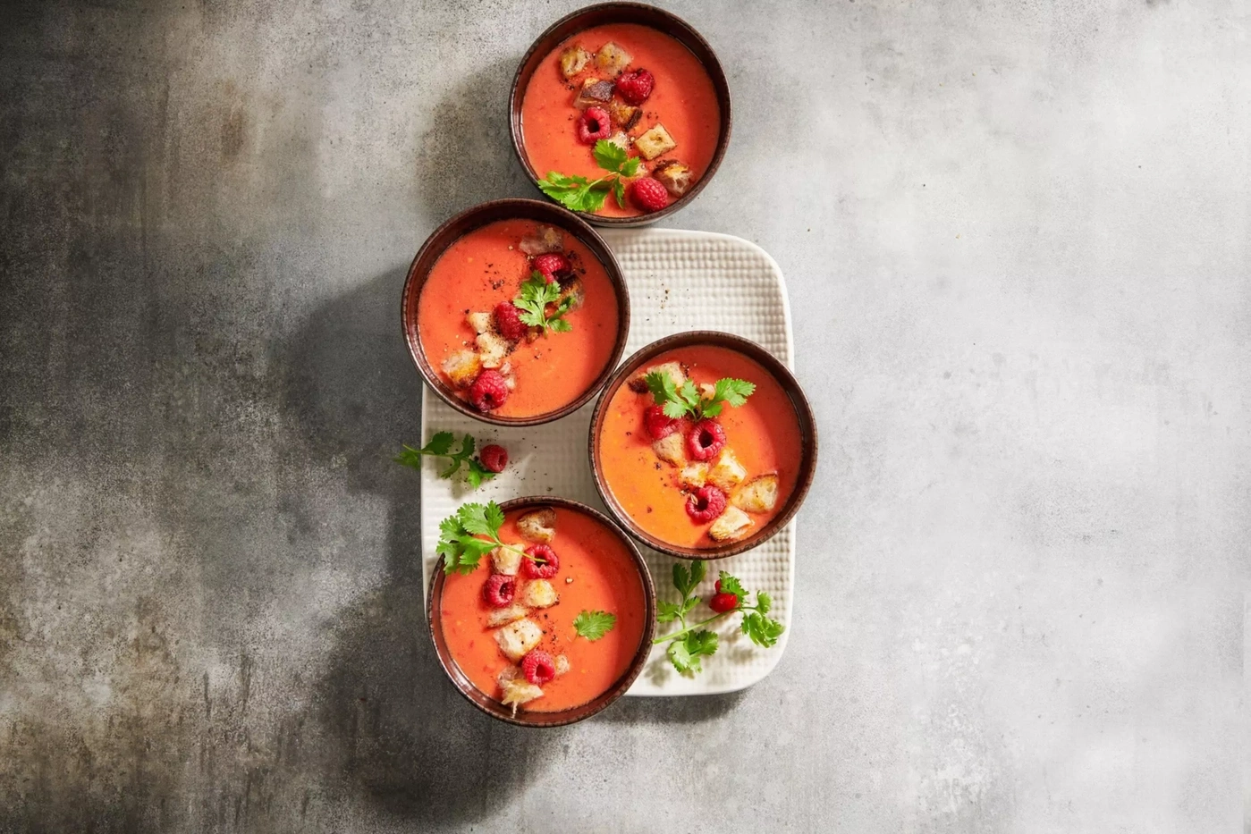 Vier Schalen Gazpacho mit Beeren und Croutons auf einem Teller