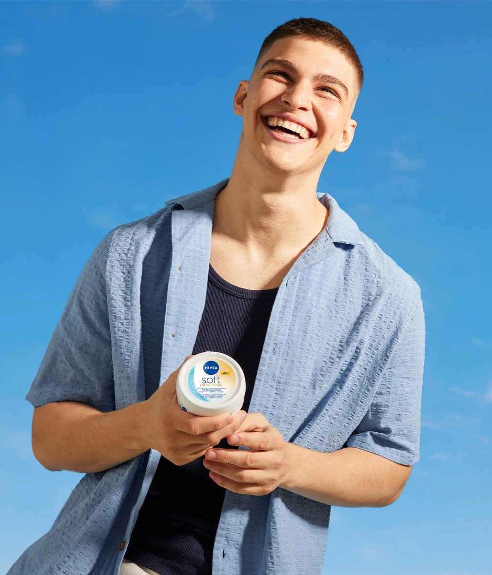 Ein Mann lacht und hält eine Nivea Soft Creme mit LSF 15.