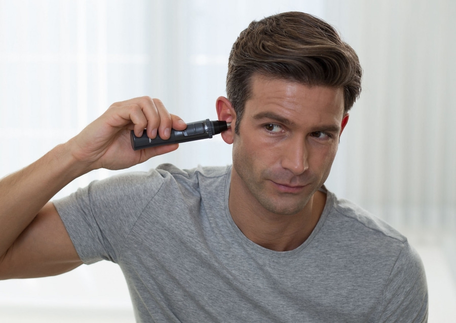 Mann rasiert sich die Ohren mit einem elektrischen Trimmer. Nahaufnahme.