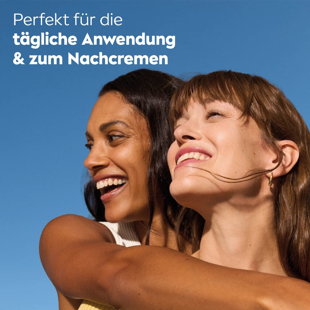 Zwei lächelnde Frauen umarmen sich vor blauem Himmel. Glückliche Gesichter.