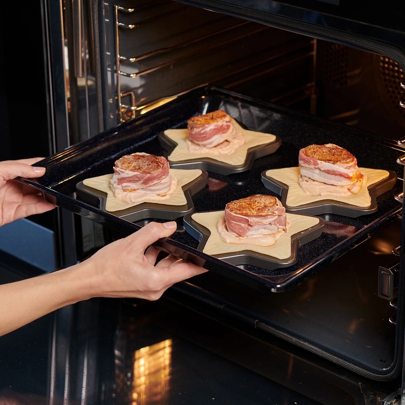 Person legt Backblech mit Fleisch in den Ofen. Sterne, Speck, Küche.