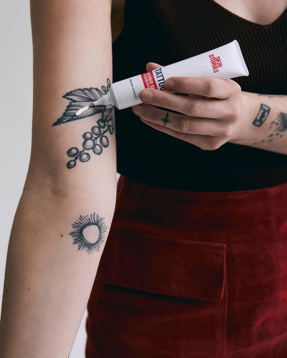 Person trägt Tattoo-Reparaturcreme auf ein Tattoo auf dem Arm auf