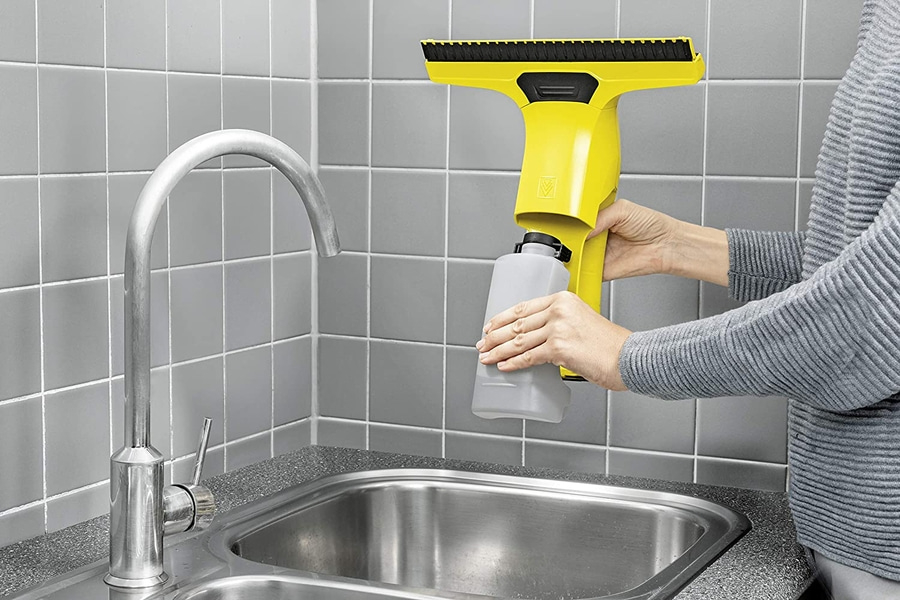 Person hält gelbes Fensterputzgerät über einem Waschbecken in der Küche.