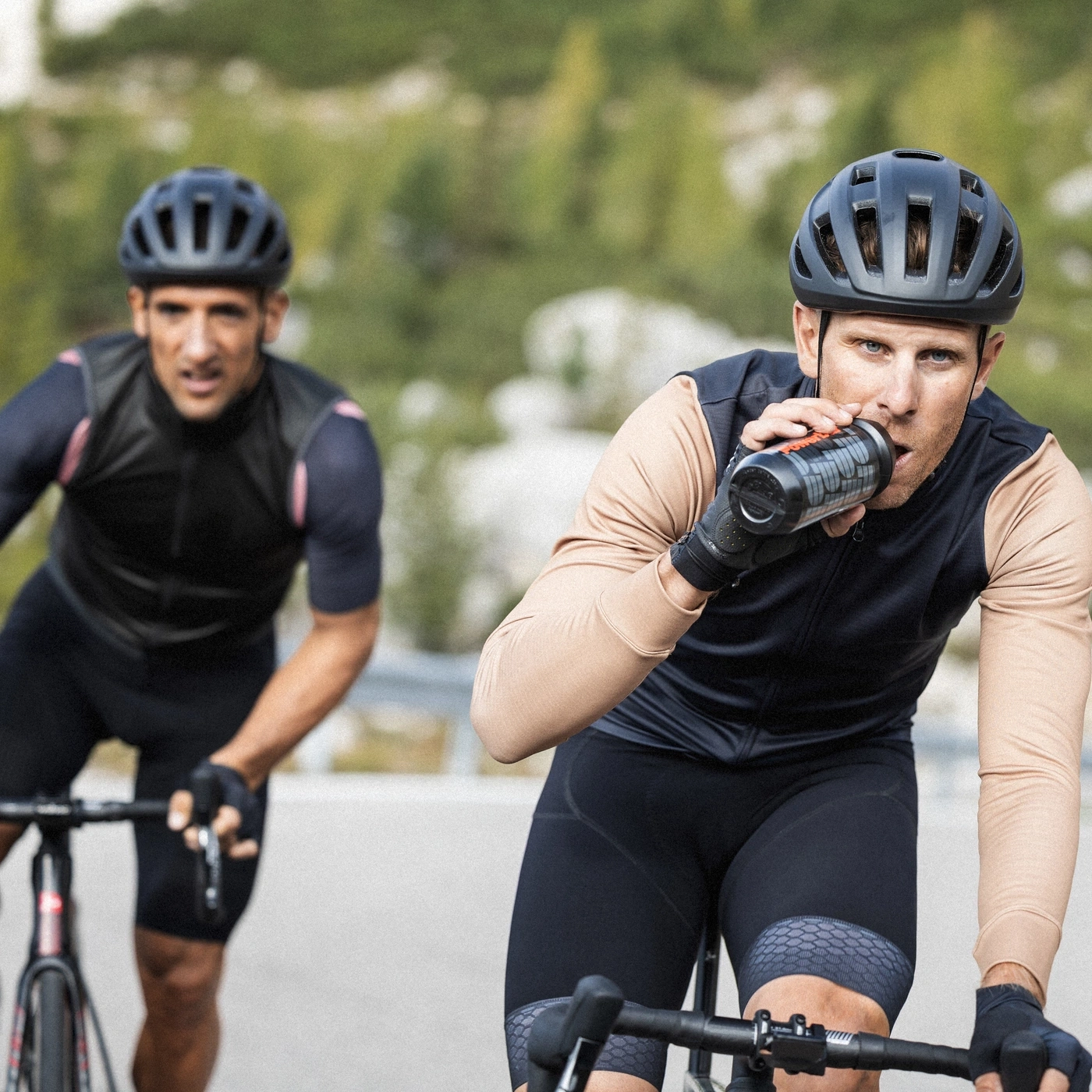 Zwei Radfahrer auf einem Hügel, einer trinkt aus einer Flasche.