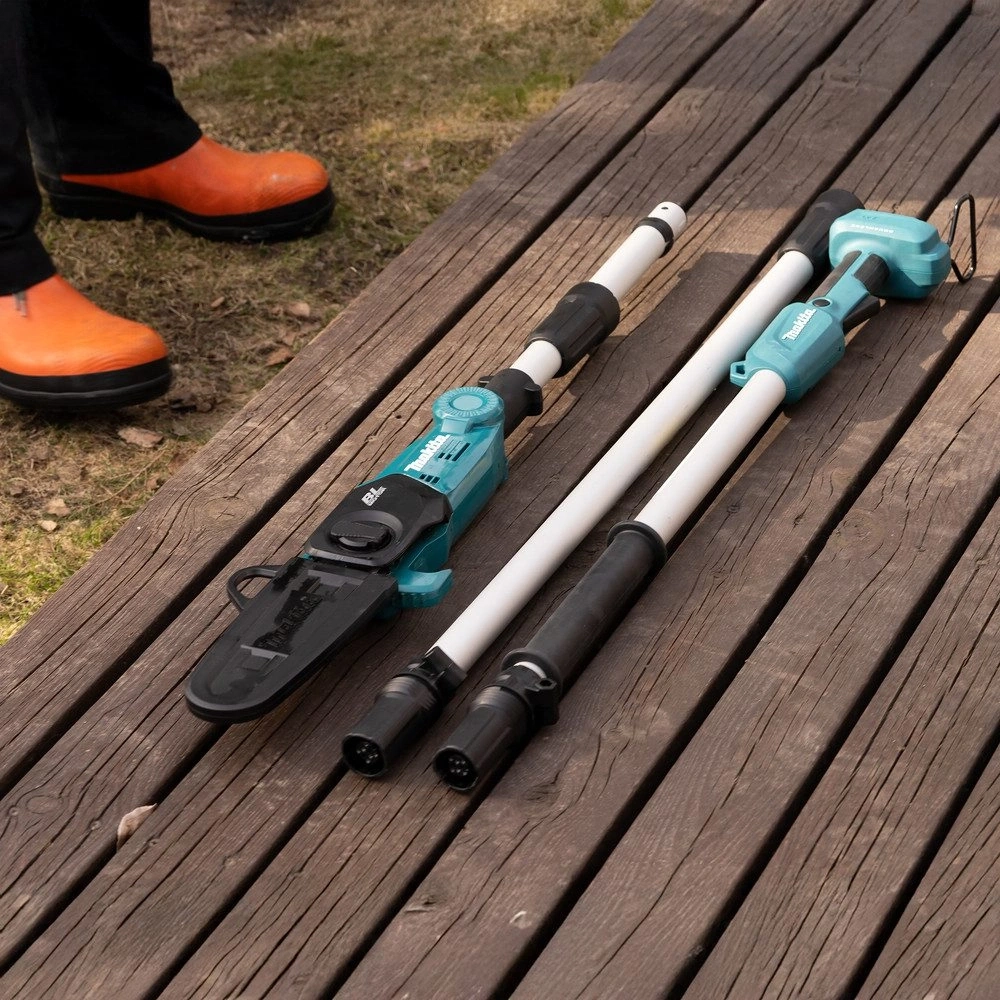 Zwei Makita Gartengeräte liegen auf einer Holzterrasse. Ein Mann trägt orangefarbene Gummistiefel.