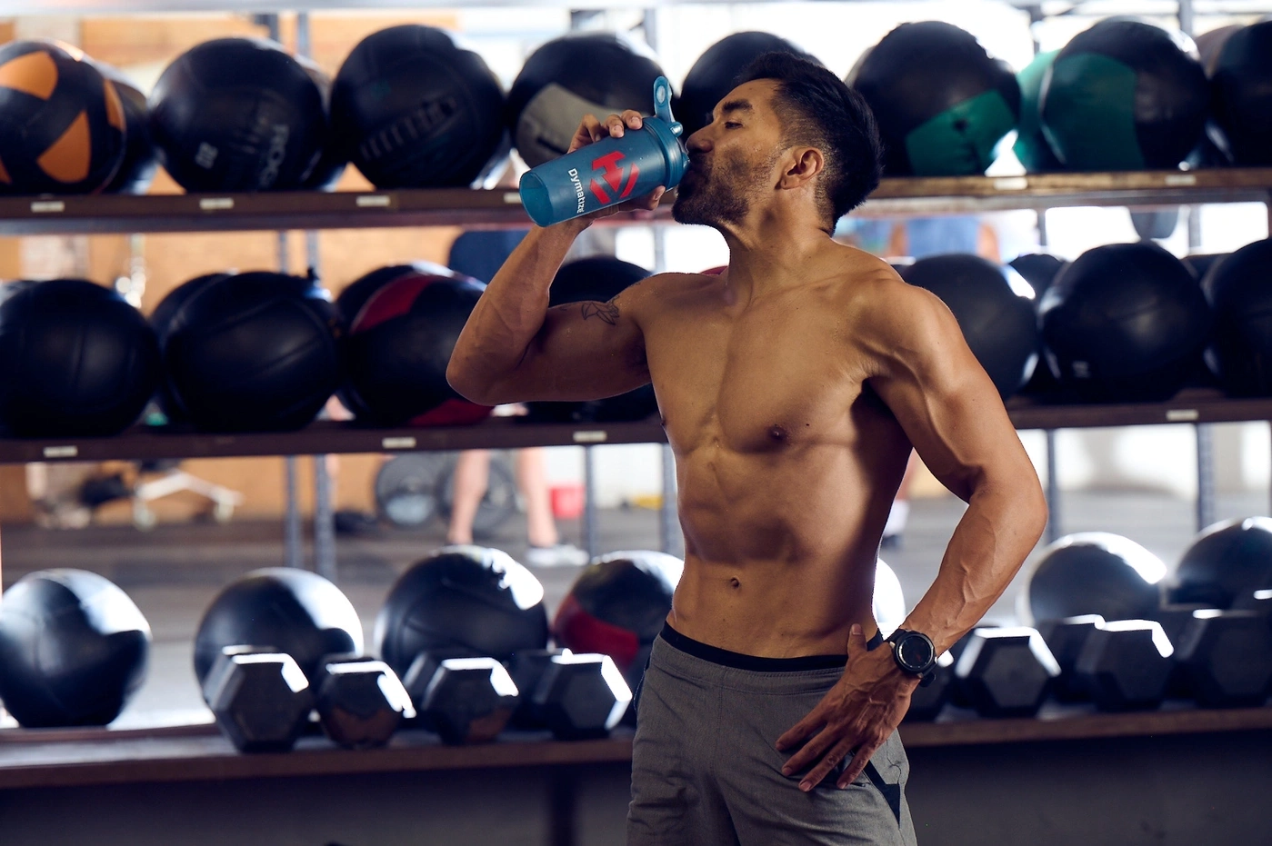 Muskulöser Mann trinkt aus einer Flasche im Fitnessstudio, Sportler