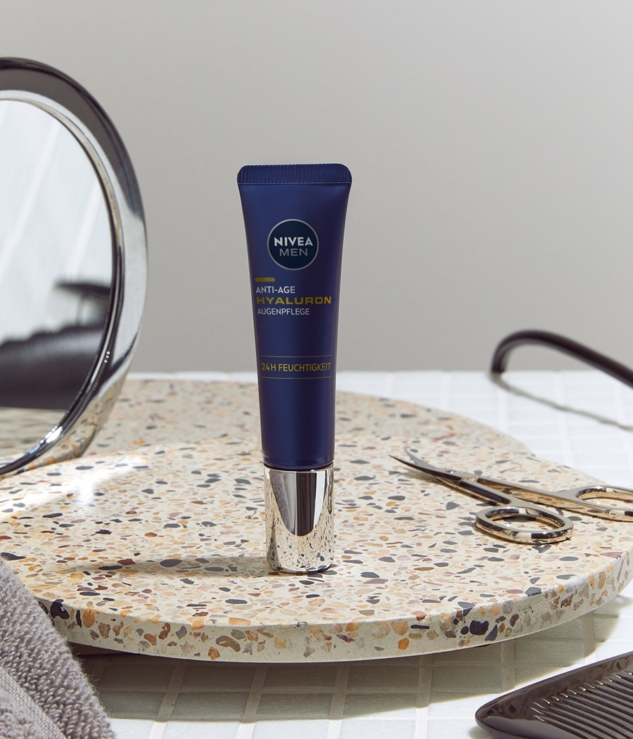Nivea Men Anti-Age Hyaluron Augenpflege Tube auf einer Oberfläche mit Spiegel und Schere