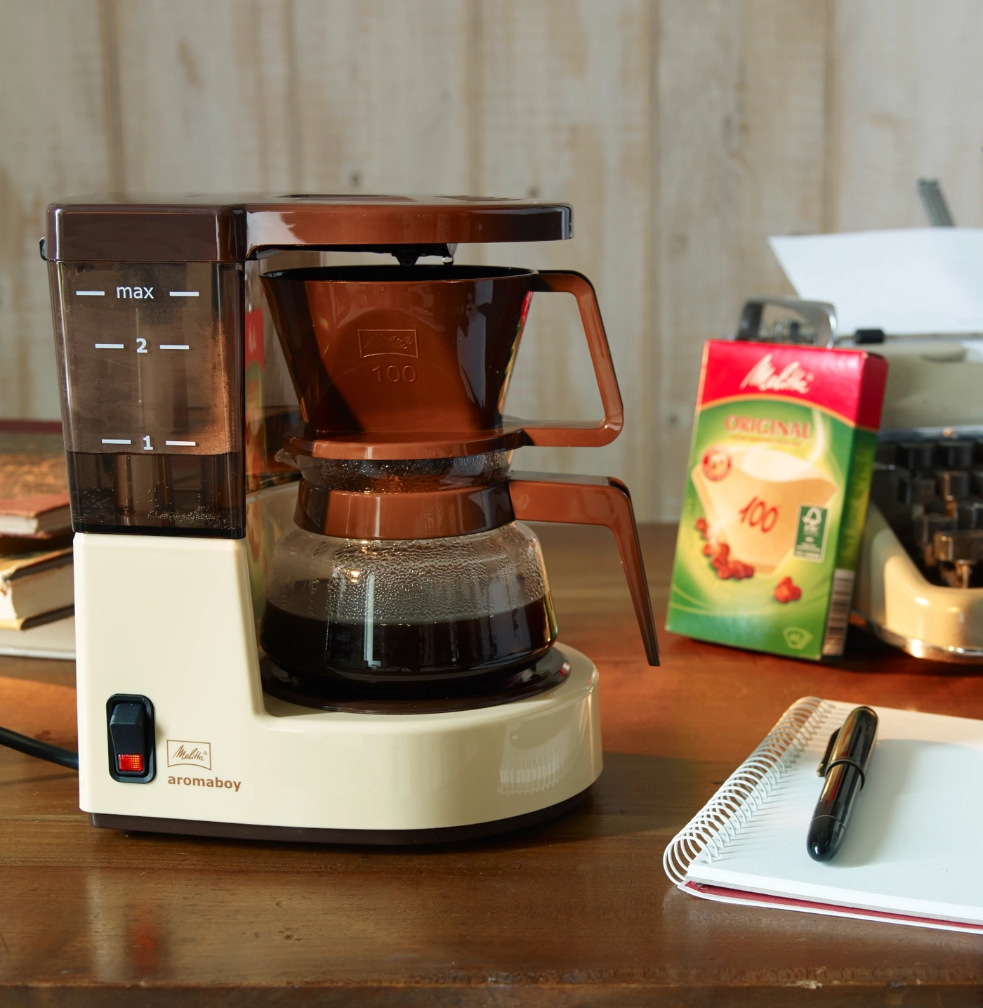 Kaffeemaschine mit Wasserbehälter, Filterhalter und Kanne auf einem Holztisch.