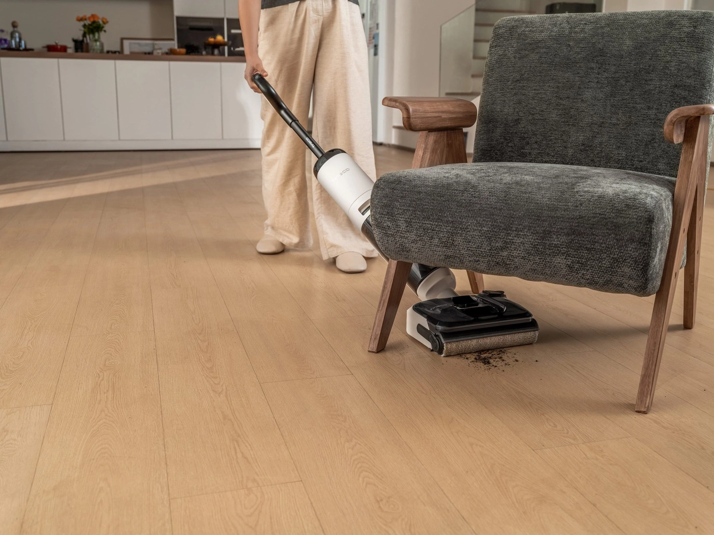 Eine Person saugt mit einem weißen Staubsauger auf einem Holzboden.