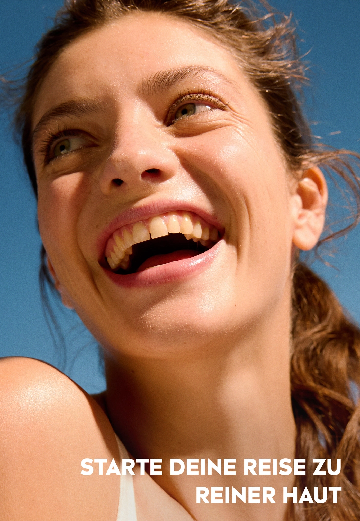 Junge Frau lacht mit reinem Hautbild vor blauem Himmel