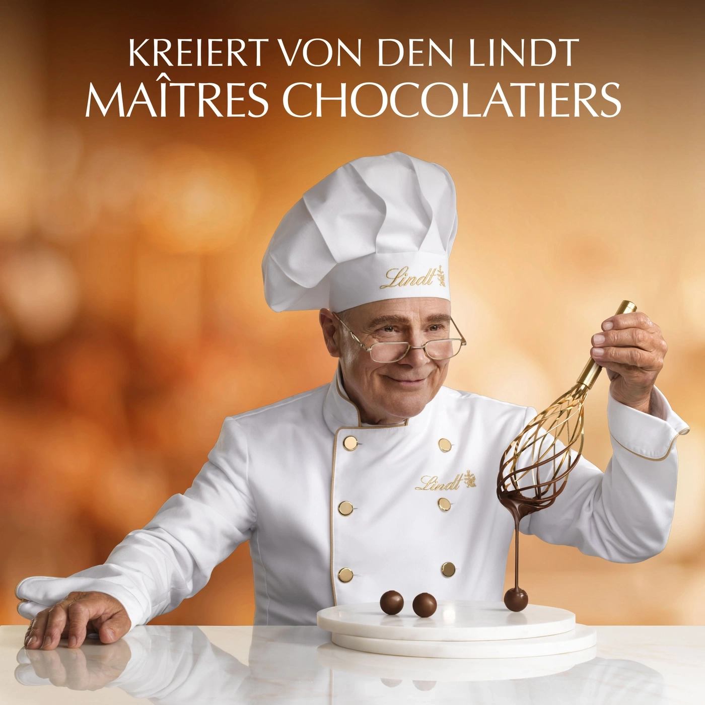 Ein Lindt Maître Chocolatier mit Kochmütze und Schürze hält einen Schneebesen mit Schokolade.
