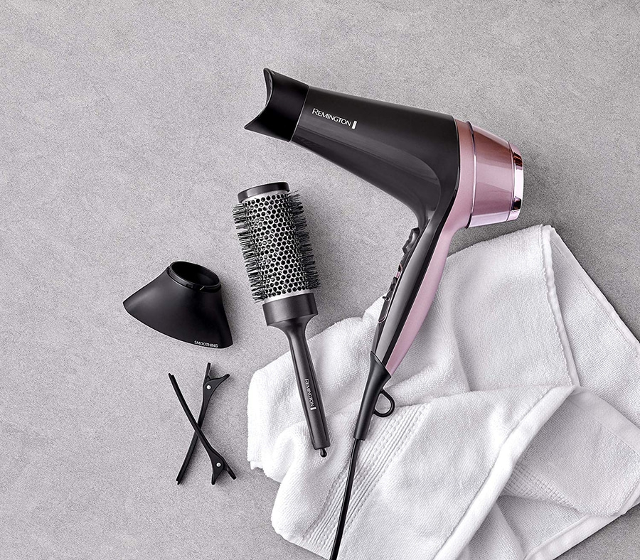 Haartrockner mit Zubehör auf weißem Handtuch, grauem Hintergrund