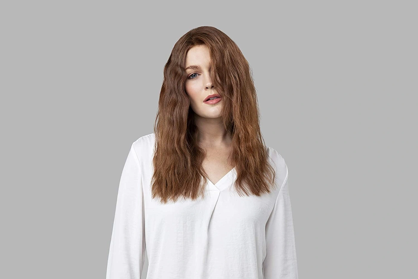 Frau mit braunen Haaren und weißem Hemd vor grauem Hintergrund