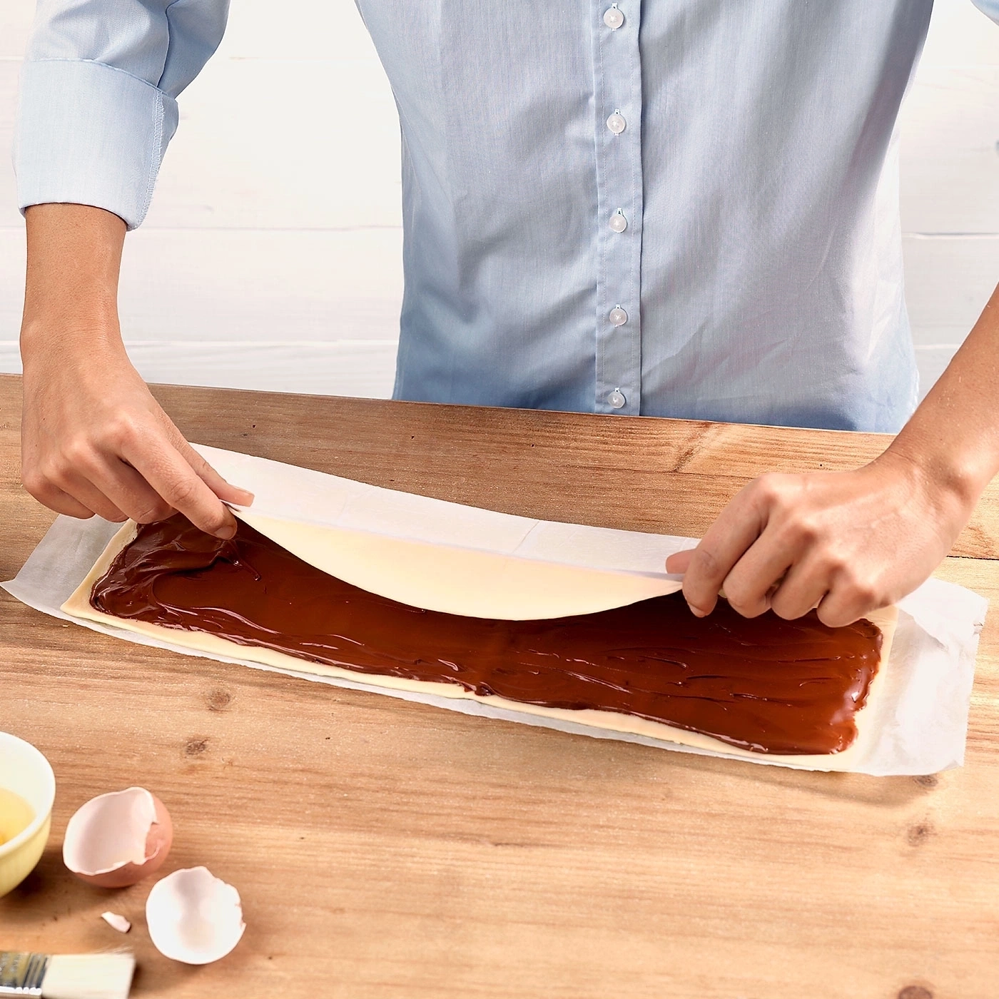 Person rollt Gebäck mit Schokoladenfüllung auf einem Holztisch ein.