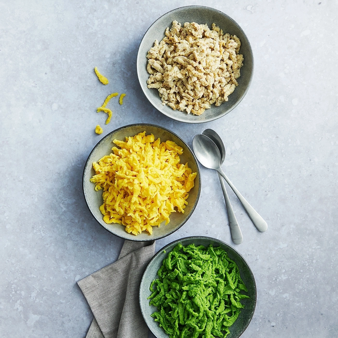 Drei Schüsseln mit Spätzle: eine mit hellen, eine mit gelben und eine mit grünen Spätzle.