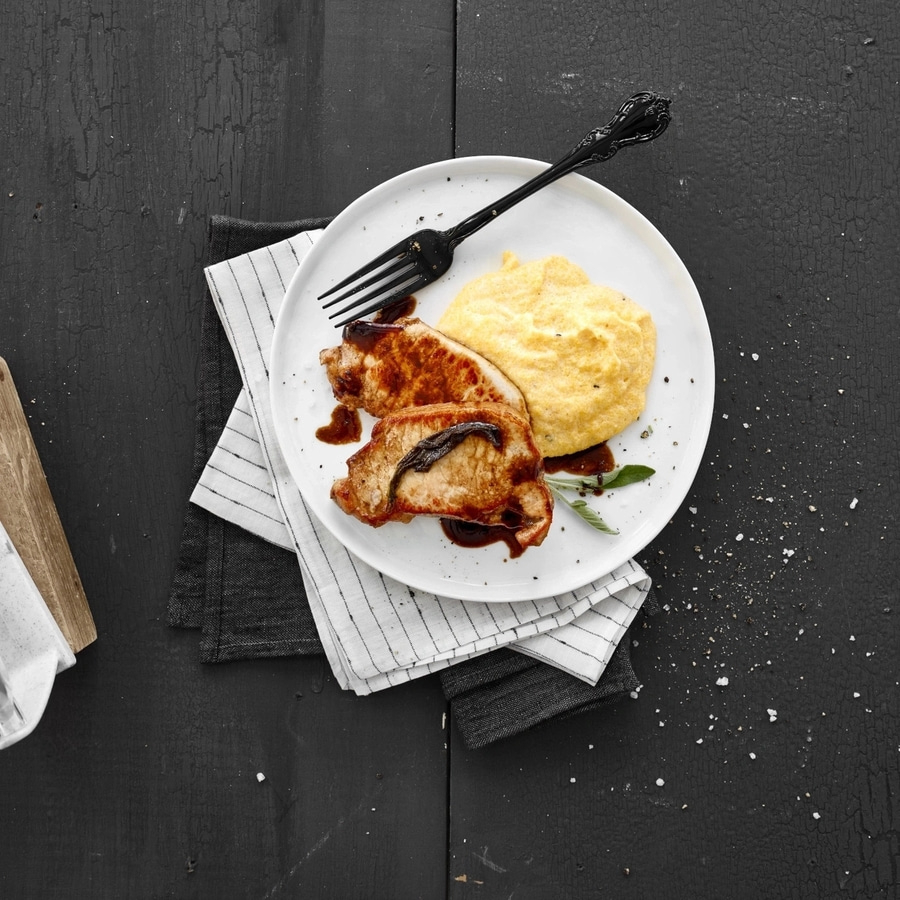 Teller mit Fleisch, Polenta und Soße auf einem schwarzen Tisch