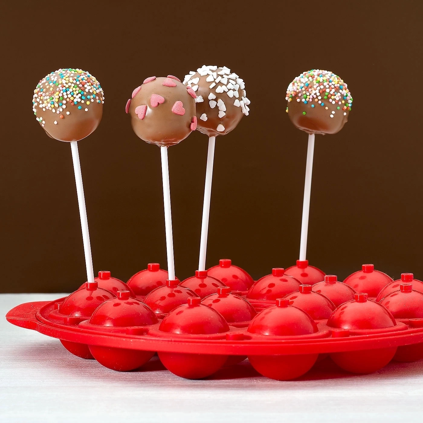 Köstliche Cake Pops auf Stielen, dekoriert mit Streuseln und Herzen, in roter Form.
