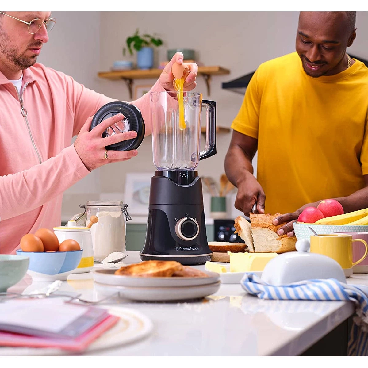 Zwei Männer bereiten Essen zu, mit einem Mixer und Zutaten auf dem Tisch.