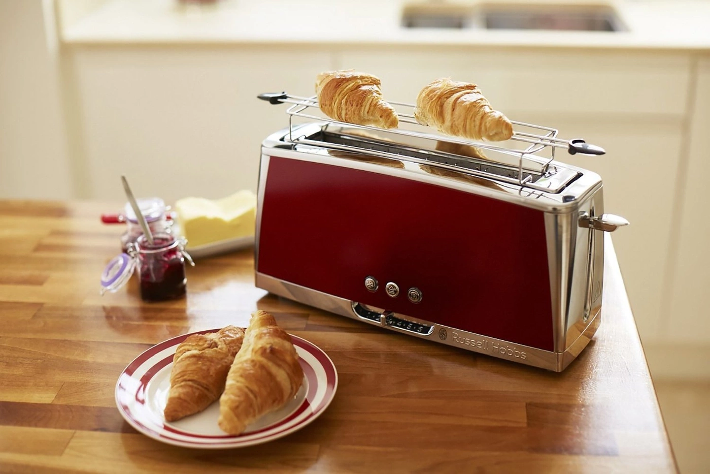 Ein roter Toaster mit Croissants, Marmelade und Butter auf einem Holztisch.