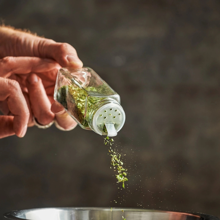 Hand hält Gewürzstreuer, Kräuter fallen in eine Schüssel, Nahaufnahme