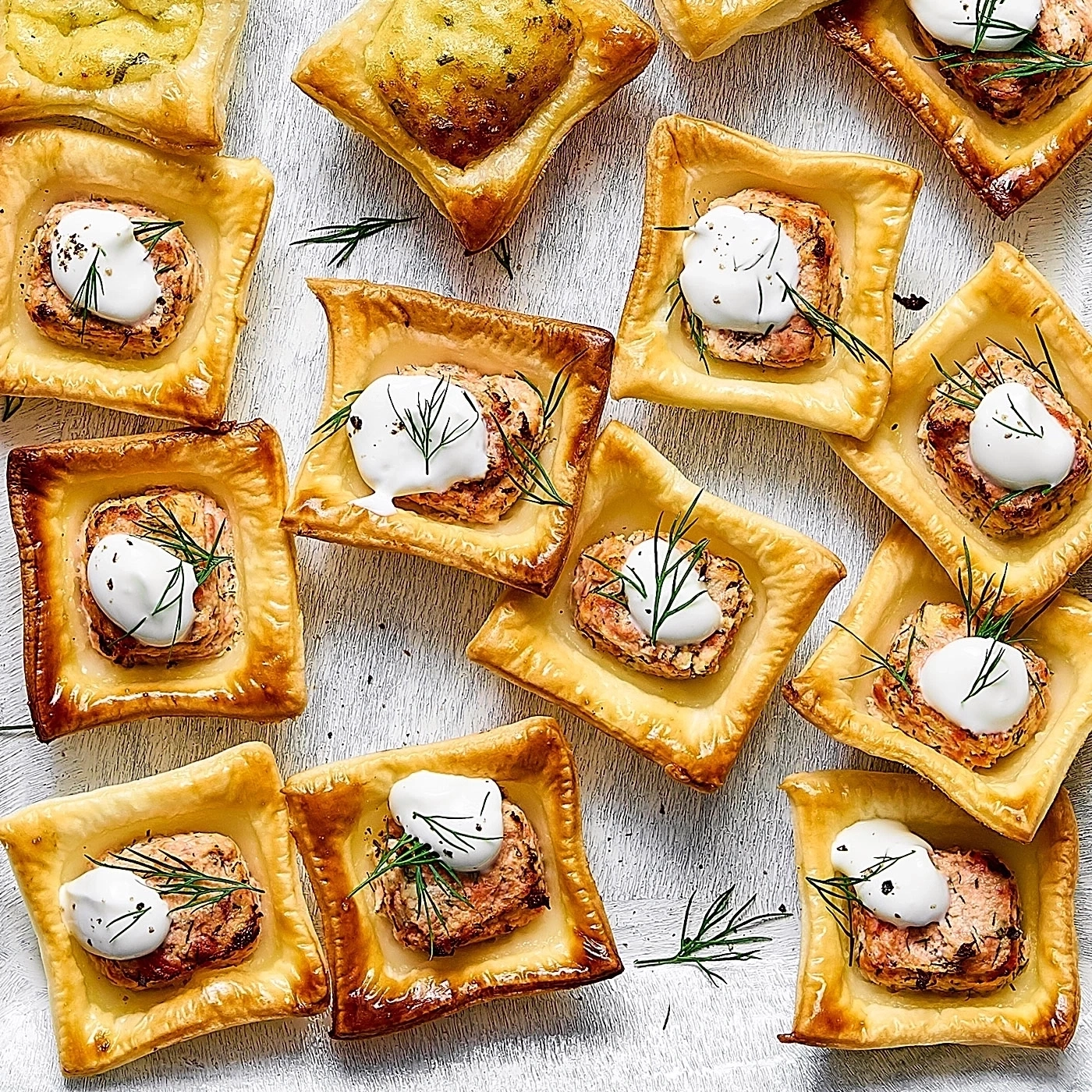 Köstliche Blätterteig-Häppchen mit Lachs, Sahne und Dill auf weißem Untergrund.