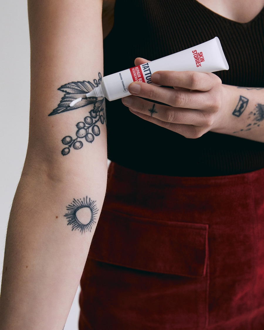 Person trägt Tattoo-Reparaturcreme auf ein Tattoo auf dem Arm auf