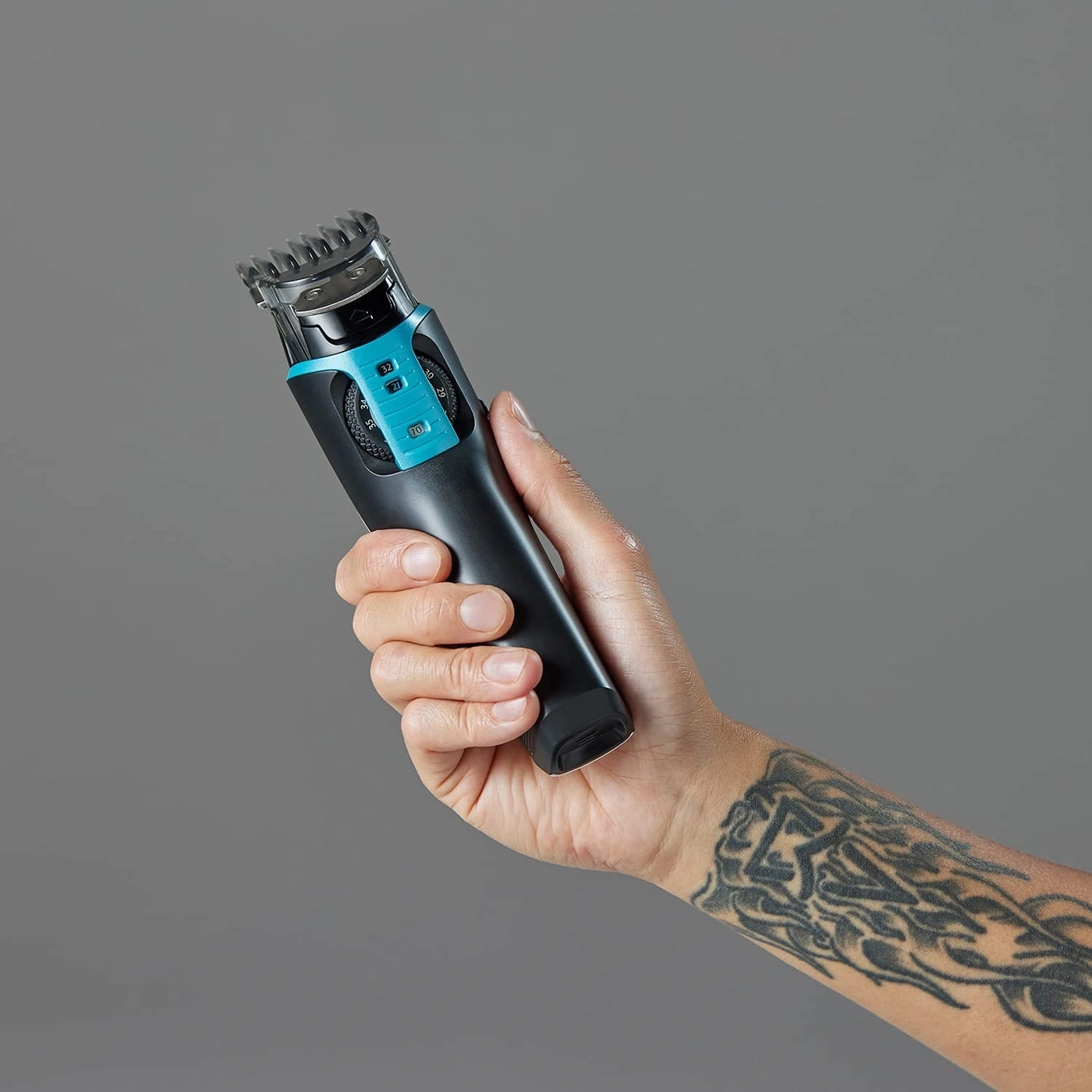 Person hält einen schwarzen Haarschneider mit blauen Akzenten und Tattoo