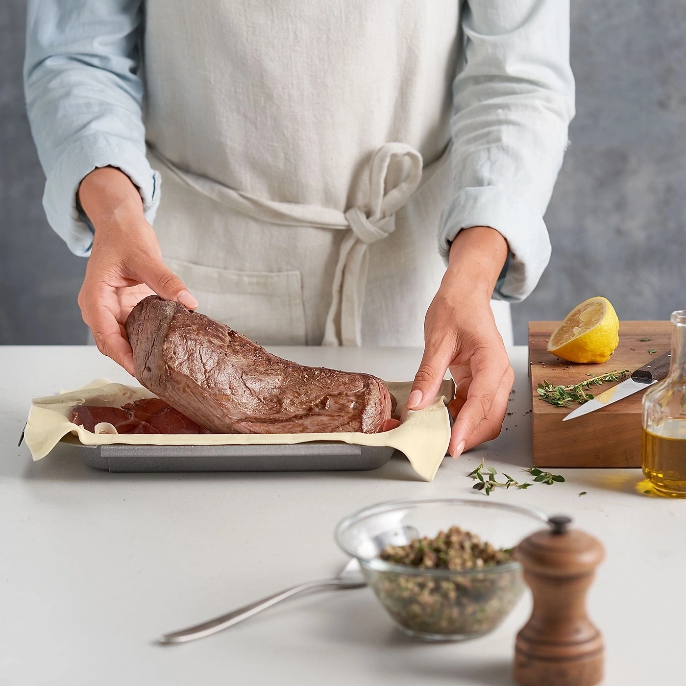 Person bereitet Fleisch zu. Zutaten: Zitrone, Kräuter, Öl, Pfeffer, Teig, Backform.