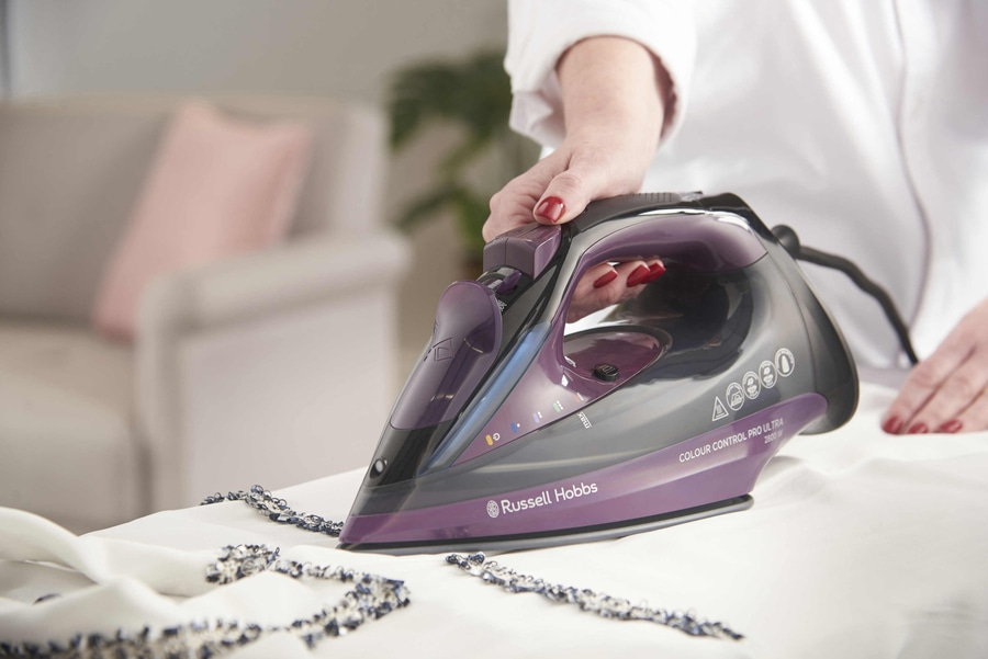 Bügeln mit einem Bügeleisen von Russell Hobbs auf weißem Stoff. Frau bügelt.