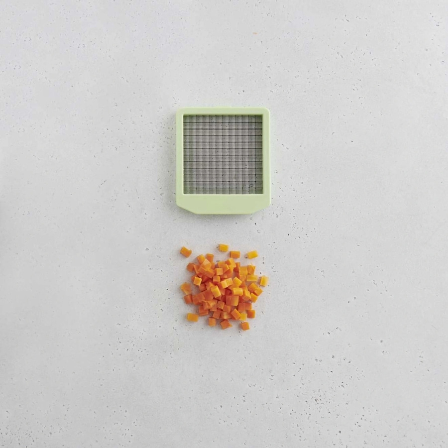 Karottenwürfel und ein grüner Gemüseschneider auf weißem Hintergrund