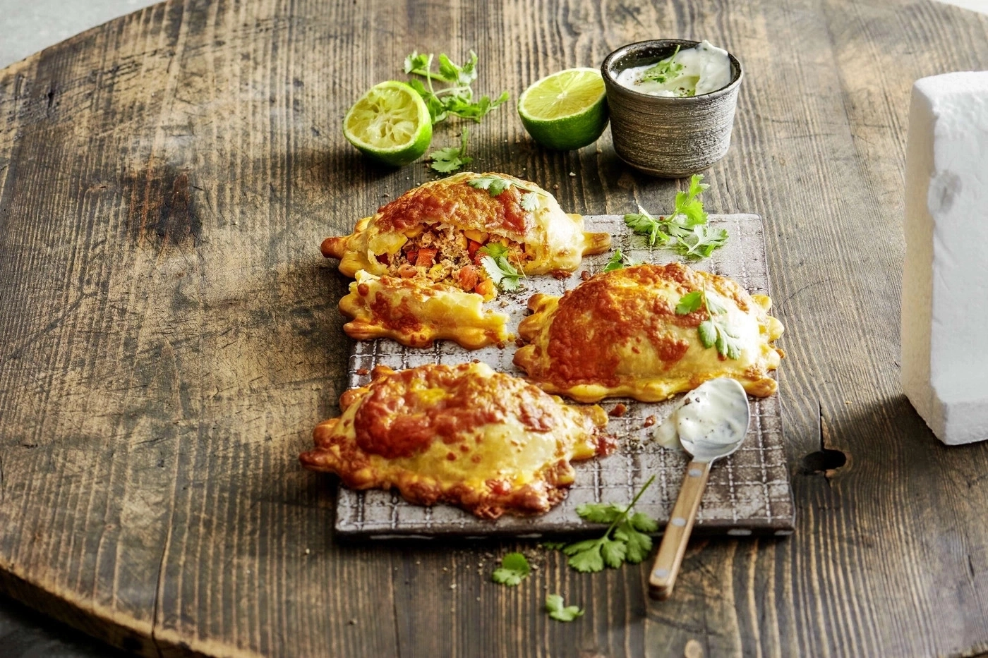 Empanadas auf einem Holzbrett mit Limetten, Kräutern und Dip