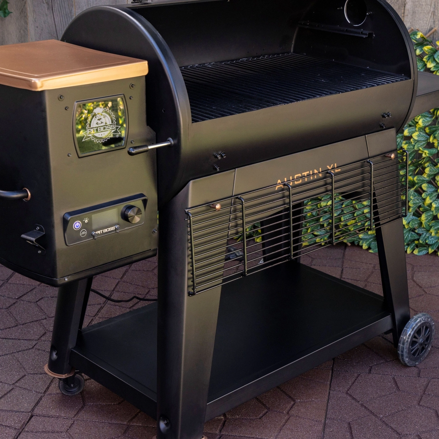 Schwarzer Pit Boss Grill mit Kupferdeckel und digitaler Steuerung auf gepflastertem Untergrund.
