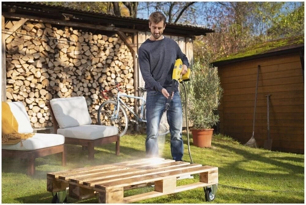 Mann reinigt Holzpalette mit Hochdruckreiniger im Garten, sonniges Wetter