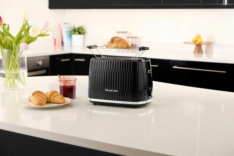 Schwarzer Toaster mit Croissant, Blumen und Marmelade auf einer weißen Oberfläche.