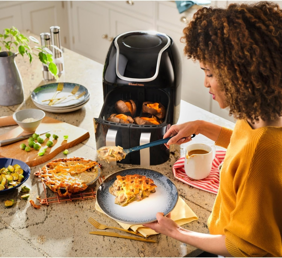 Frau serviert Essen aus der Heißluftfritteuse, mit Kuchen und Gemüse.