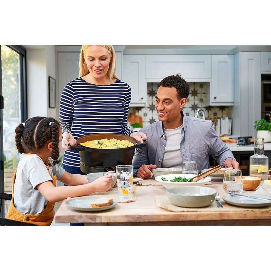 Familie isst gemeinsam am Tisch. Mutter serviert Essen, Vater und Kind sitzen.