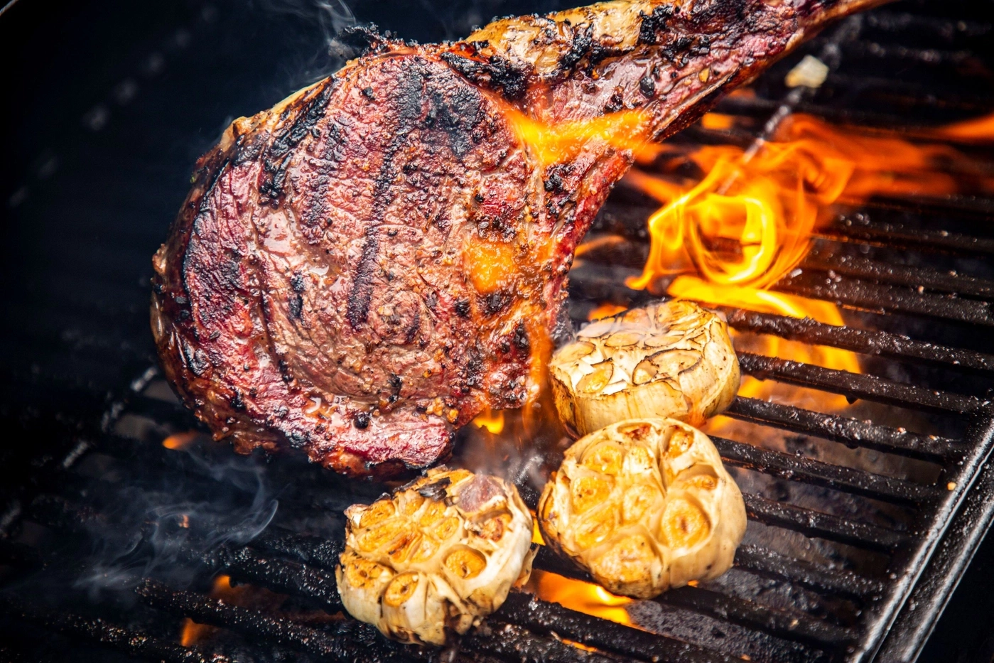 Ein saftiges Steak mit Knoblauch auf einem Grill mit Flammen.
