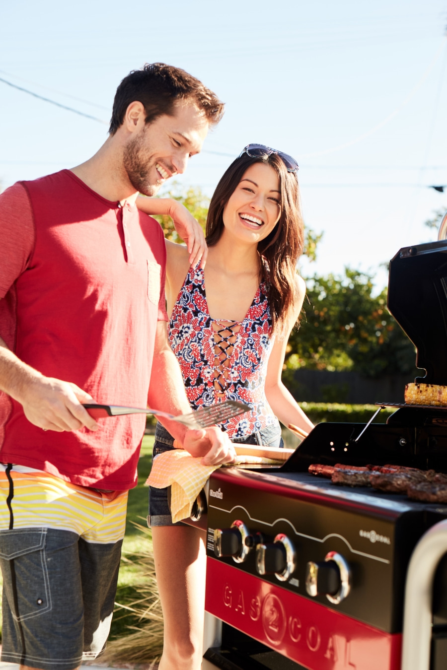 Ein lächelndes Paar grillt im Freien, Sommer, Essen, Freude, Glück, Grillen, Mann, Frau, Sonne