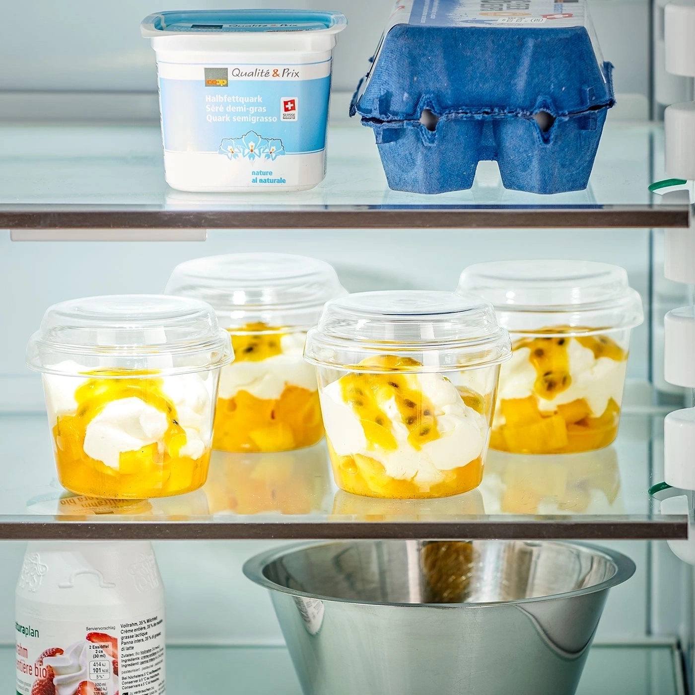 Kühlschrank mit Joghurt, Eiern und Dessertbechern mit Obst und Sahne.