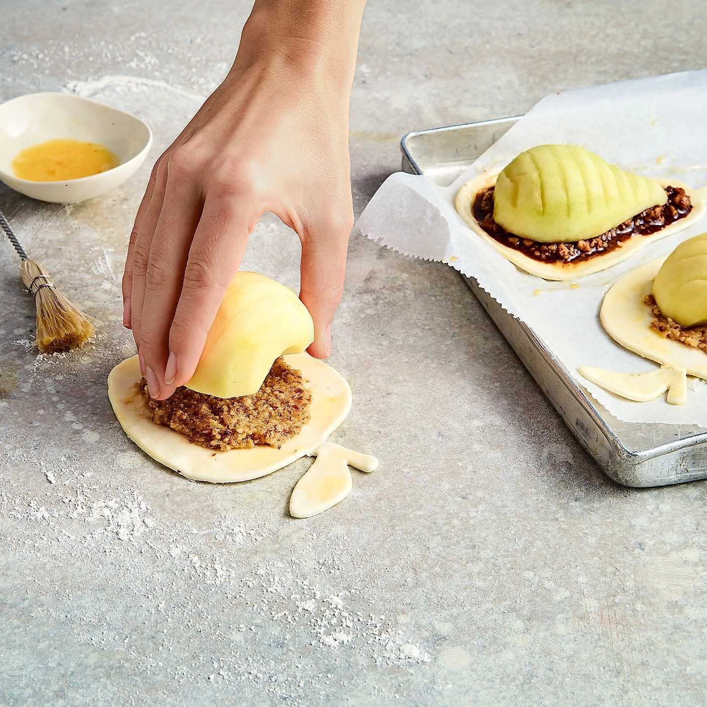 Hand legt Apfel auf Teig mit Füllung, Backblech mit Birnen