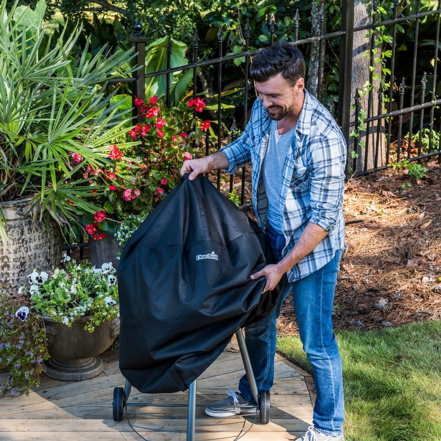 Mann deckt Grill ab, lächelt, Garten, Holzterrasse, Blumen, Zaun, sonniger Tag