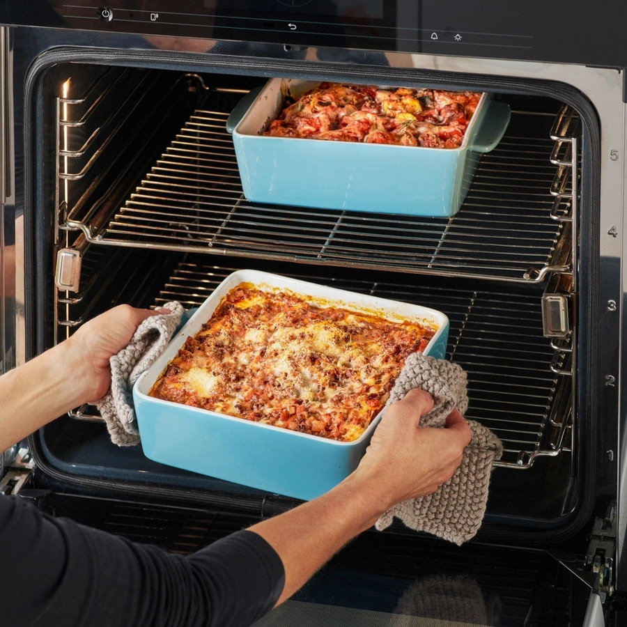 Ofen mit Aufläufen. Person nimmt Auflauf aus dem Ofen. Leckeres Essen.