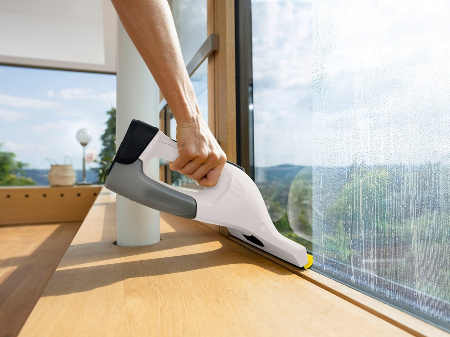 Person reinigt Fenster mit einem Fensterreiniger. Sauberes Fenster, Ausblick auf die Natur.