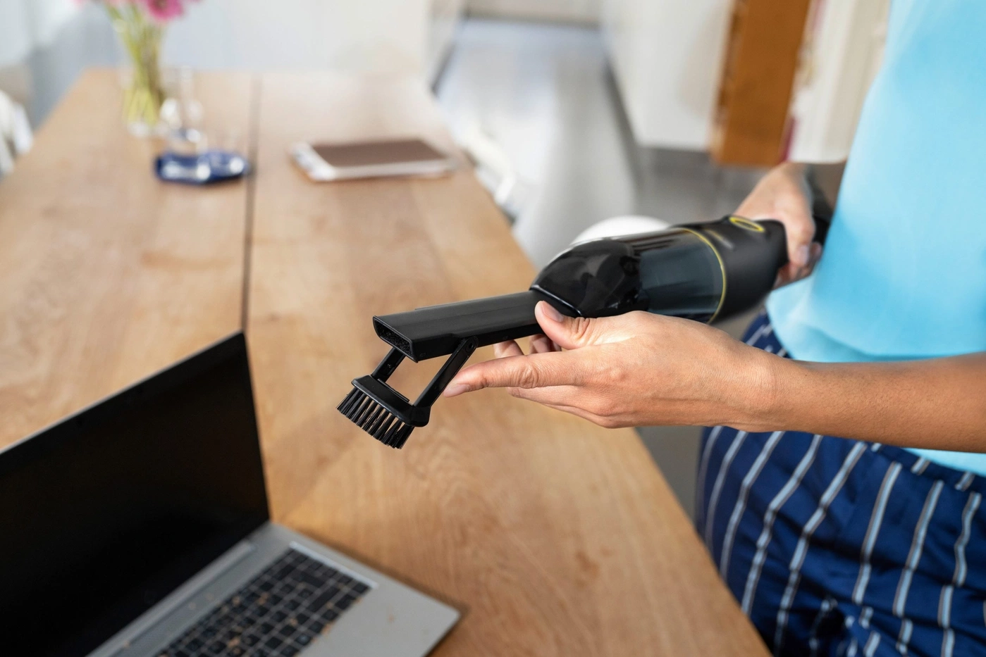 Hand hält Staubsauger mit Bürstenaufsatz auf Holztisch