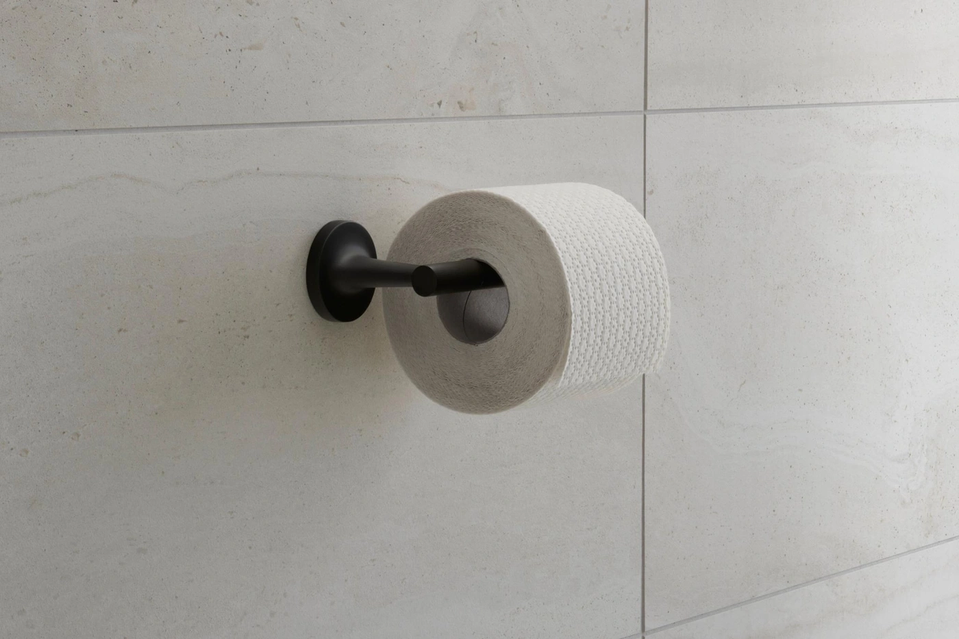 Toilettenpapierhalterung mit Rolle vor hellen Fliesen. Schwarze Halterung.